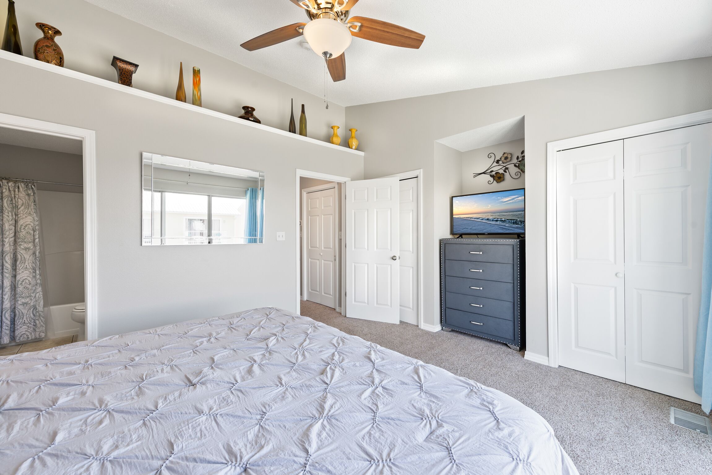 A bedroom with a bed, a ceiling fan, a dresser, a TV, and a closet.