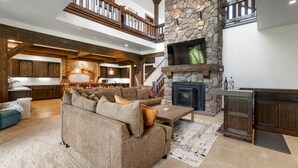 A spacious living area with a stone fireplace, wooden beams, and a cozy seating arrangement.