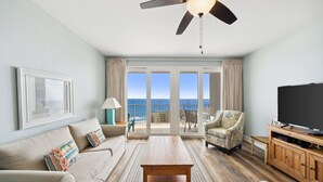 A living room with a sofa, armchair, coffee table, TV, and a ceiling fan.