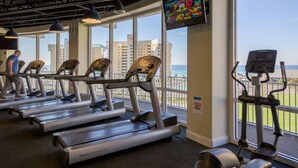 A gym with multiple treadmills, a television mounted on the wall, and large windows overlooking a cityscape.