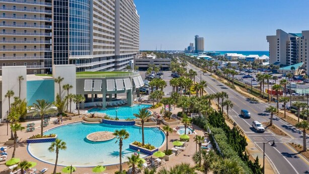A hotel with a large pool, palm trees, and a view of the ocean.