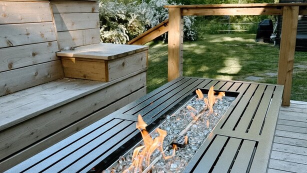 Een terras met een ingebouwde vuurplaats, houten traptreden en een pergola.