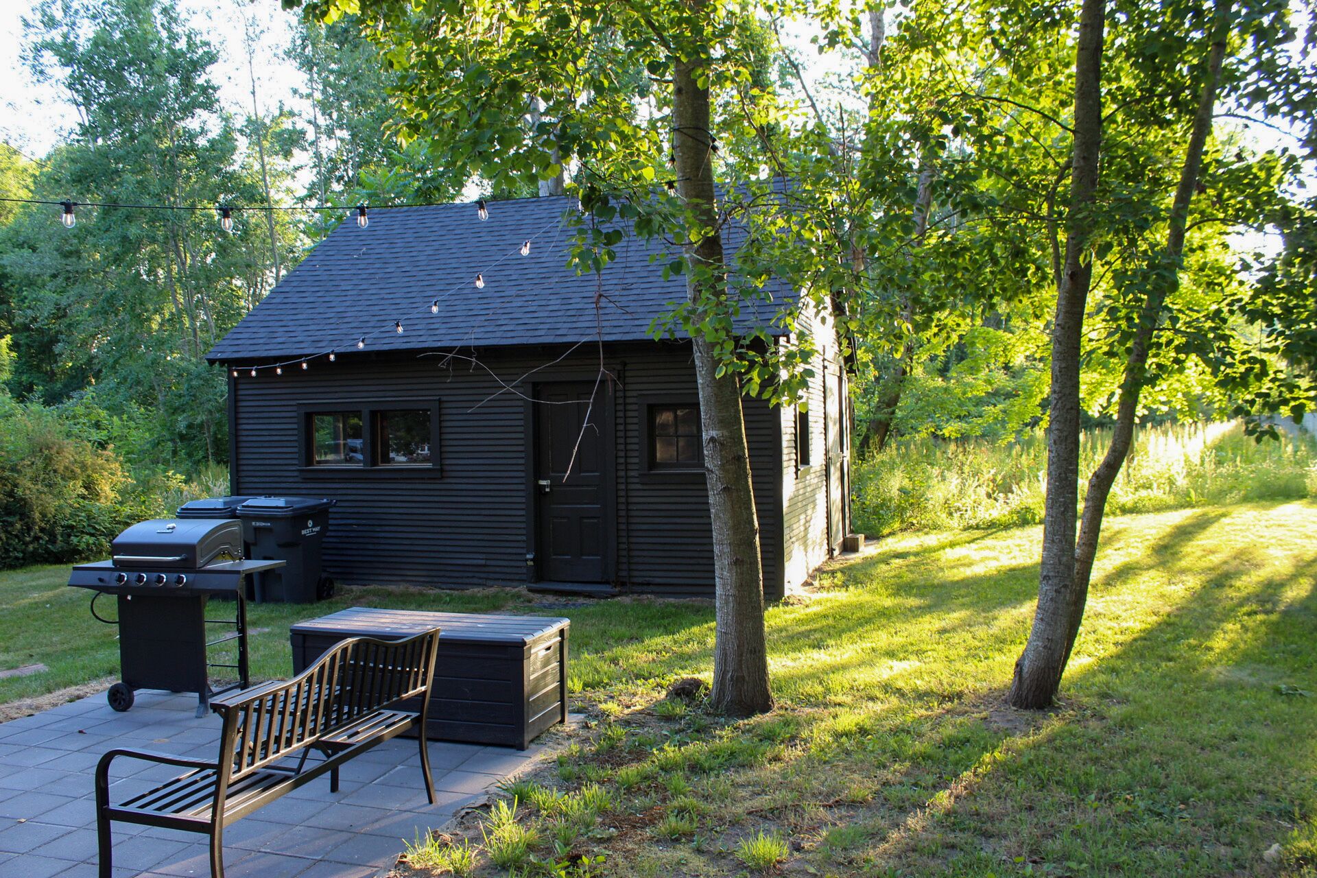 A small cabin with a grill and a bench outside.