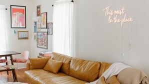 Een moderne woonkamer met een hoekbank, een klein rond tafeltje en een roze fauteuil.