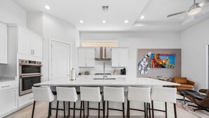 A modern kitchen with white cabinetry, a central island with bar stools, and a dining area with a brown sofa.
