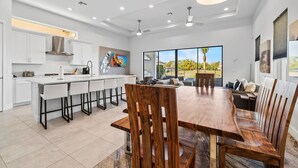 A modern kitchen with white cabinetry, a wooden dining table, and a large window offering a view of the outdoors.