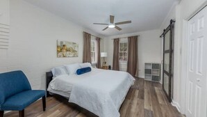 Un dormitorio con una cama, una silla, un ventilador de techo y un cuadro en la pared.