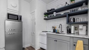 Una cocina moderna con un refrigerador de acero inoxidable, armarios blancos, un horno empotrado y un microondas. Hay repisas negras sobre la encimera con varios utensilios de cocina.