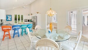 Une cuisine moderne avec des meubles blancs, un réfrigérateur en acier inoxydable et un coin repas comprenant une table en verre et des chaises en osier.
