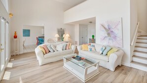 Un salon spacieux avec deux canapés blancs, une table basse en verre et un escalier.