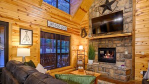 A cozy log cabin interior with a stone fireplace, leather sofa, and a sign that reads "Life is so good".