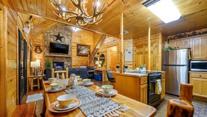 A wooden cabin interior with a dining area, kitchen, and living space.