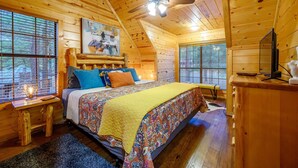 A cozy cabin bedroom with a bed, wooden walls, a ceiling fan, and a painting on the wall.