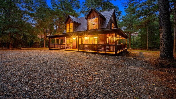 A log cabin with a porch and large windows, surrounded by trees.