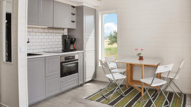 Una cocina compacta con gabinetes grises, una cafetera y vistas al exterior a través de un ventanal grande.