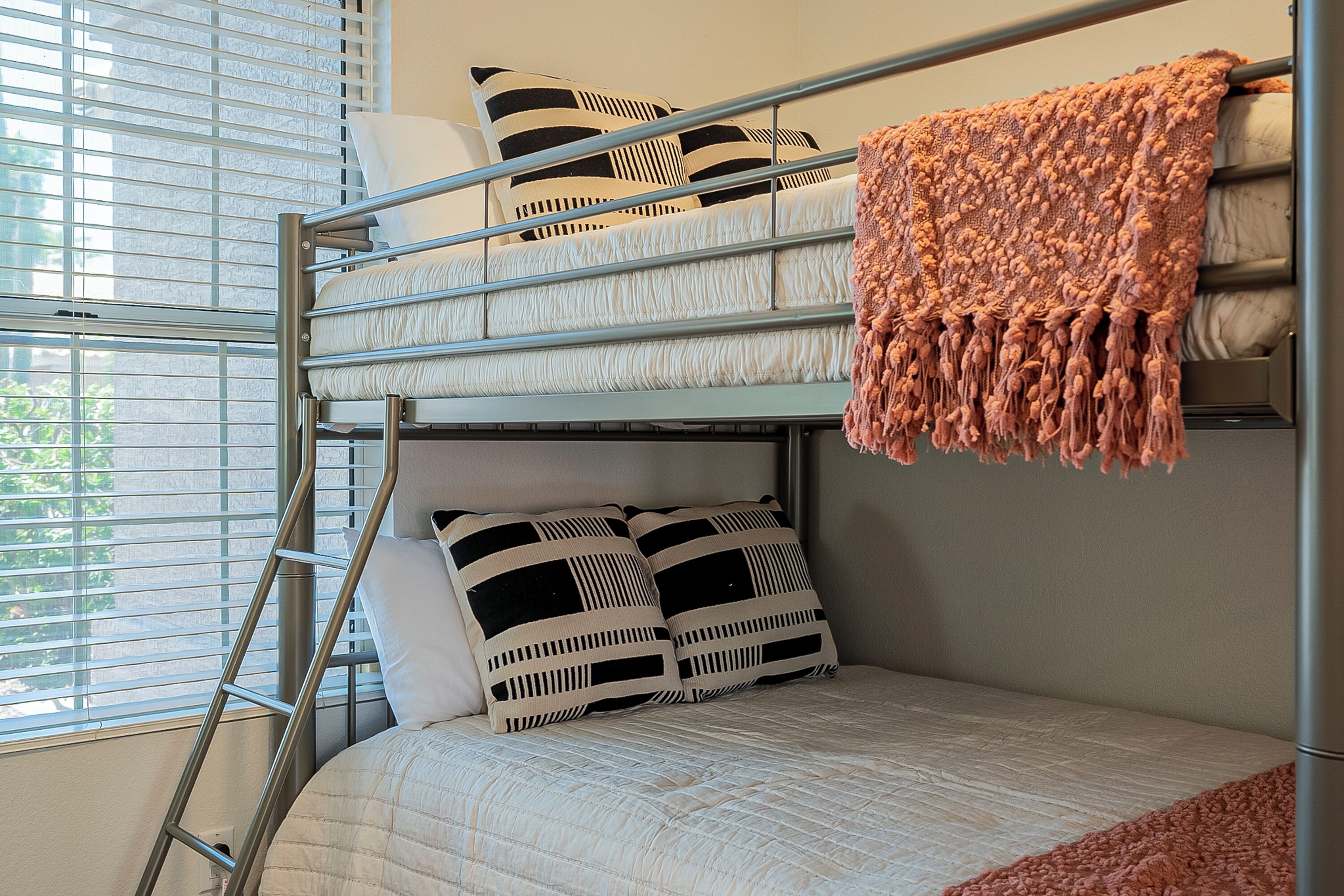Uma cama beliche com escada, dois travesseiros preto e branco e um cobertor cor de pêssego.