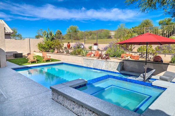 A swimming pool with a blue mosaic border, surrounded by a stone deck, and equipped with lounge chairs and a red umbrella.