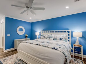 Ein Schlafzimmer mit einem Bett, zwei Nachttischen, einem Deckenventilator und einem an der Wand befestigten Spiegel.