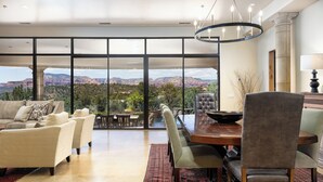 Amplia sala de estar con una gran mesa de comedor, asientos cómodos y vistas a montañas a través de amplias ventanas.