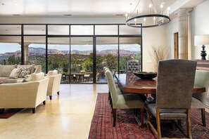 A spacious living area with a large dining table, comfortable seating, and a view of mountains through large windows. - 2024 VRBO Property of the Year: Palatial Paradise w/ Infinity Pool, Spa & Incredible Red Rock Views (Sedona)