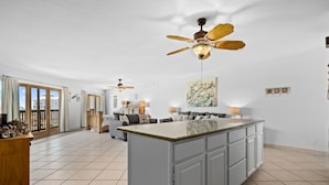 A spacious kitchen with a central island, a dining area with a sofa, and a ceiling fan.