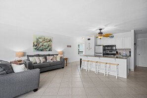 En moderne stue med en grå sofa, et køkken med hvide skabe og en loftventilator.