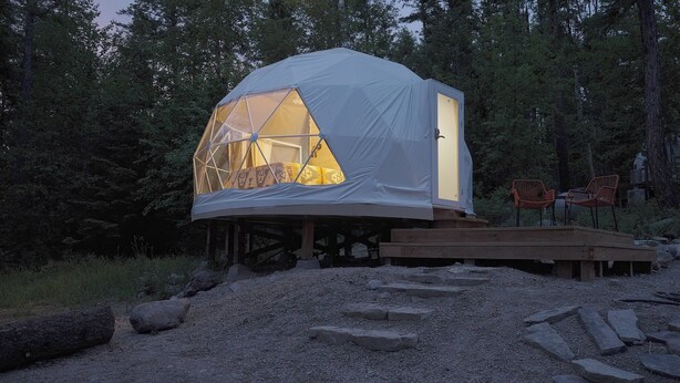 A geodesic dome structure with a transparent section, wooden deck, and surrounding forest. - Red Owl Retreat-The Nook. (Bigfork)