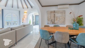 A modern dining area with a wooden table and chairs, a large abstract painting on the wall, and a view of the sea through a large window. - CostaBlancaDreams - Villa Paraguana in Benitachell (Benitachell)