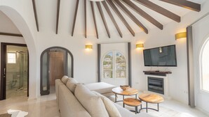 A modern living room with a sofa, two wooden tables, a fireplace, and a TV mounted on the wall. - CostaBlancaDreams - Villa Paraguana in Benitachell (Benitachell)