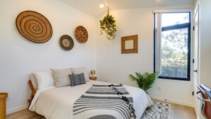 Een slaapkamer met een bed, nachtkastjes, een hangende plant en een raam met uitzicht.