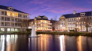 A waterfront hotel with multiple buildings, a central fountain, and a calm lake reflecting the structures.