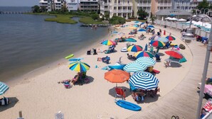 A beach with colorful umbrellas and beach chairs, a wooden boardwalk, and a row of buildings in the background.