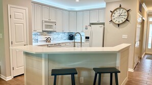 A kitchen with white cabinetry, a large island with stools, a clock, and a microwave.