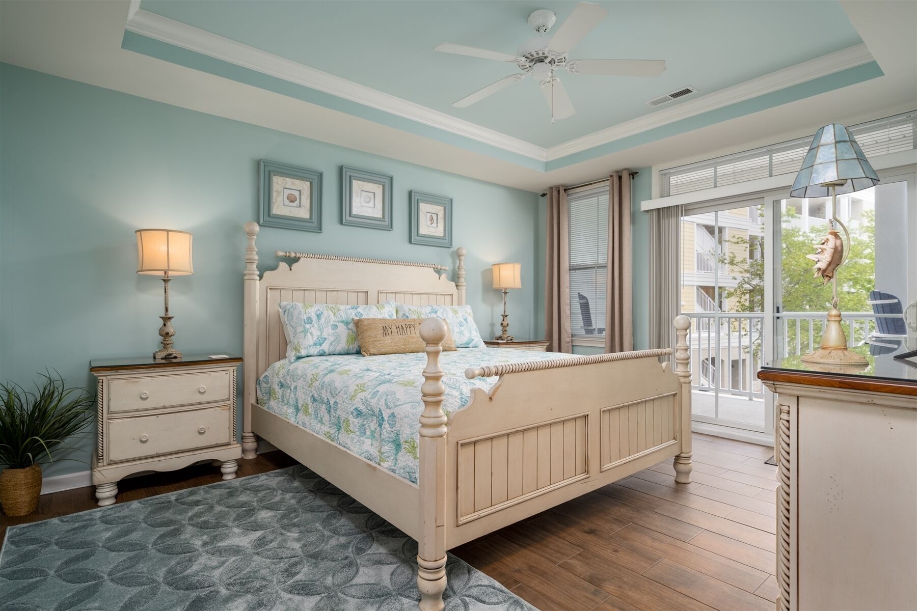 A bedroom with a bed, nightstands, a ceiling fan, and a view of the outside.