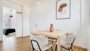 Un comedor moderno con una mesa de madera y cuatro sillas, un florero sobre la mesa, y una obra de arte enmarcada en la pared.