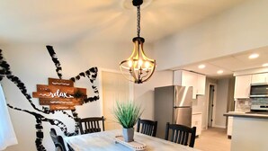 A dining area with a wooden table, black chairs, a chandelier, and a modern kitchen in the background. - Updated, Spacious, Fully Fenced Yard (Northfield)