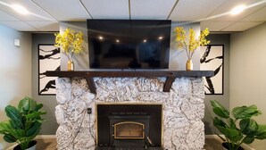 A stone fireplace with a black mantel, flanked by two potted plants, and a flat-screen TV mounted above. - Updated, Spacious, Fully Fenced Yard (Northfield)