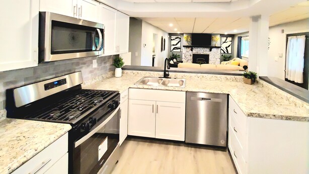 A modern kitchen with white cabinets, stainless steel appliances, a granite countertop, and a built-in dishwasher. - Updated, Spacious, Fully Fenced Yard (Northfield)