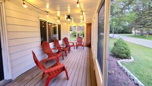 A covered porch with wooden flooring and red plastic chairs, overlooking a well-maintained lawn and trees. - Updated, Spacious, Fully Fenced Yard (Northfield)