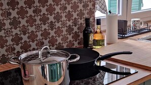 A kitchen with a black induction cooktop, a stainless steel pot, a bottle of Deja Blue, and a mug on the counter. - La Brignoletta - Le Case del Dria - Aquarium suite (Genova)