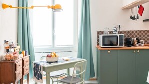 A kitchen with a microwave, coffee maker, and utensils on the counter. There is a table with a bowl of fruit and a chair. - La Brignoletta - Le Case del Dria - Aquarium suite (Genova)