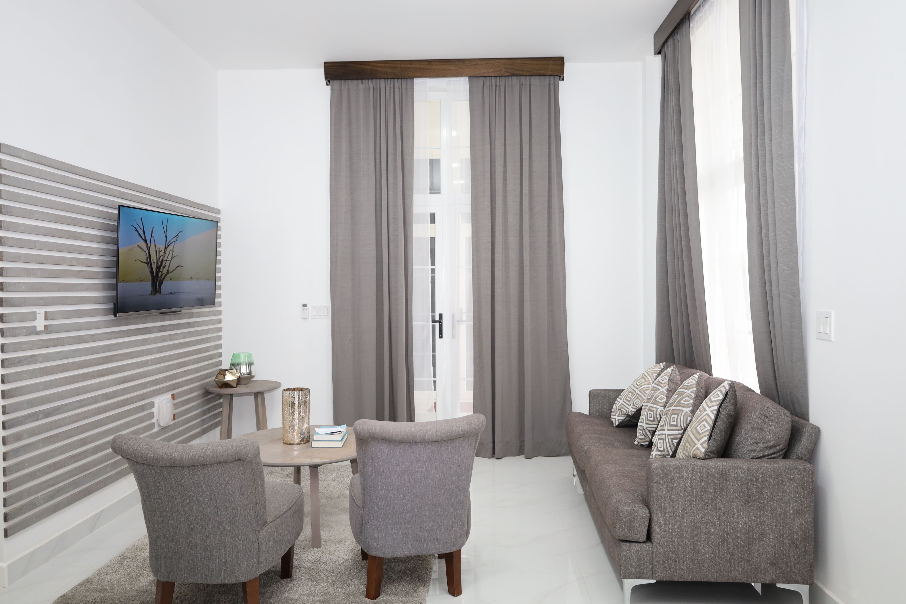 A modern living room with a grey sofa, two armchairs, a small table, and a painting on the wall.