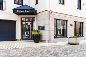 A building with a black awning labeled "Poschinger Carré" and a glass door entrance. There are two flower planters outside.