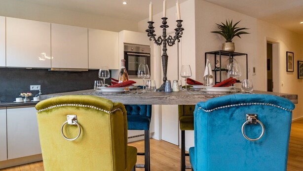 Een moderne keuken met witte kasten, een marmeren aanrecht en een eettafel gedekt met rode servetten en wijnglazen.