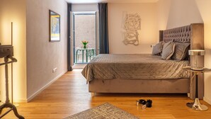 Een slaapkamer met een groot bed, een bedlampje, een klein tafeltje en een stoel.