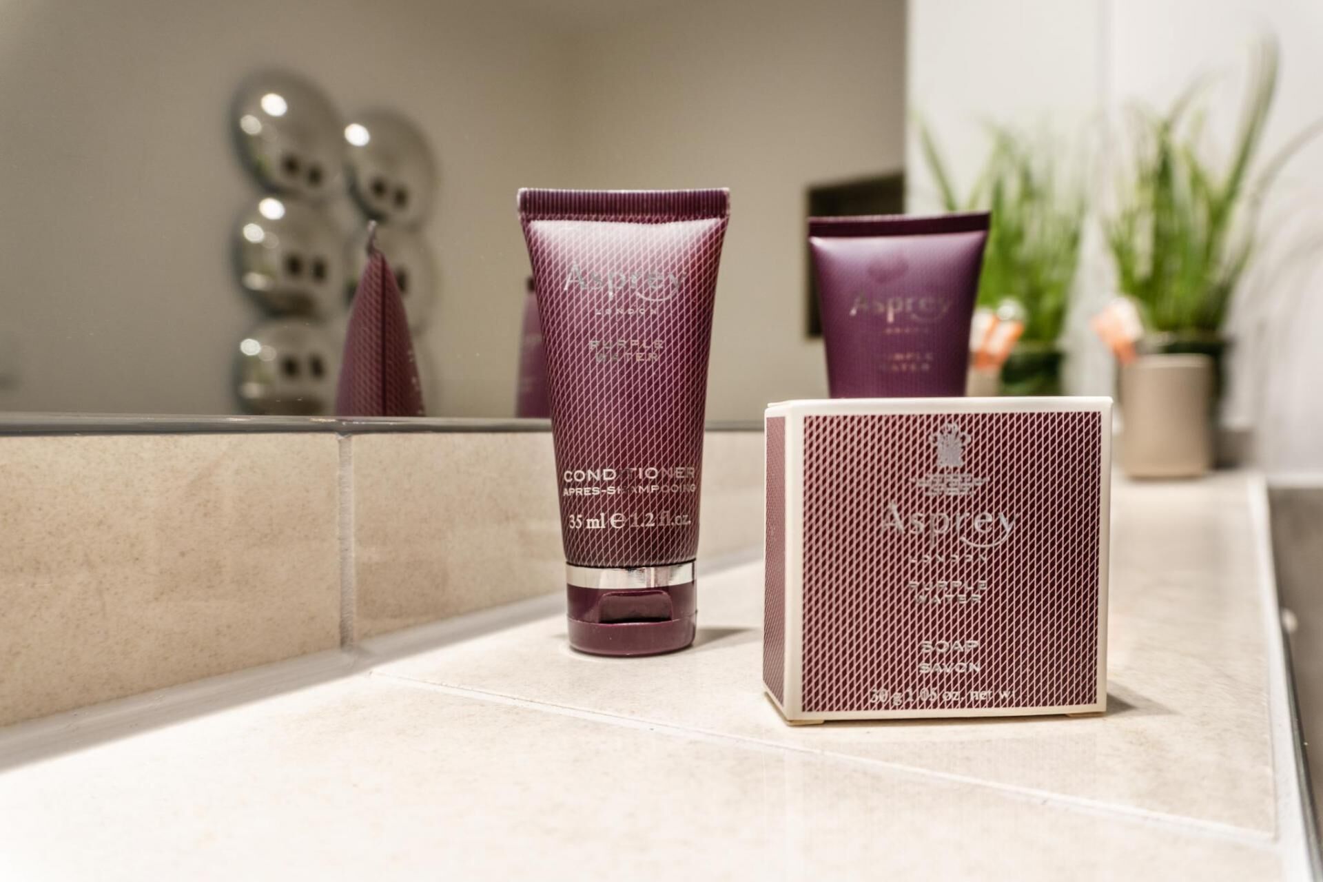 A bathroom with a mirror, a purple shampoo bottle, a purple conditioner bottle, and a purple soap bar on the counter.