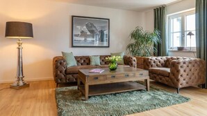 Una sala de estar con un sofá de cuero marrón, una mesa de centro de madera, una lámpara de pie, un cuadro en la pared y una planta grande.