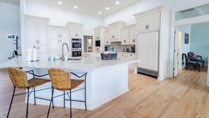 A spacious kitchen with white cabinetry, a large island with bar stools, and a dining area with a table and chairs. - Beautiful Balboa Lake Home with Stunning View (Hot Springs Village)