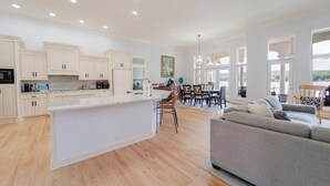 A spacious kitchen with white cabinets, a central island, and a dining area with chairs and a table. - Beautiful Balboa Lake Home with Stunning View (Hot Springs Village)