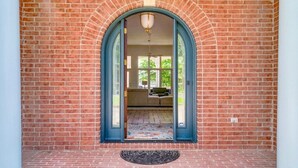 A brick exterior with a large arched doorway leading to an interior space with a tiled floor and a patterned rug. - Beautiful Balboa Lake Home with Stunning View (Hot Springs Village)